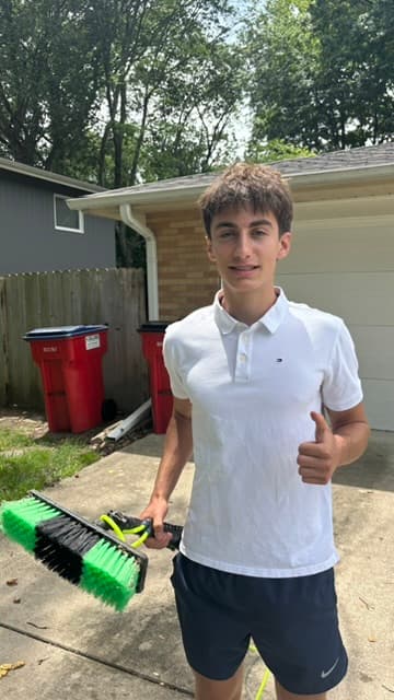 Noah Green, owner of CU Window Wash, smiling with a thumbs up and holding his window-cleaning brush in a driveway